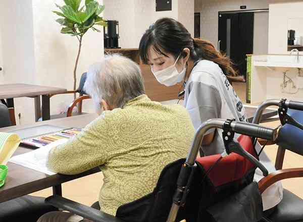 住宅型有料老人ホーム「メディケア癒やし京町台」で入所者（手前）と会話するスタッフ＝熊本市