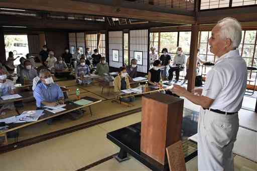 前田一洋さん（右）の講話を聴く合同例会の出席者ら＝人吉市