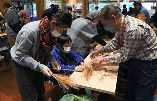 野焼きボランティアの指導でススキのミニほうき作りを体験する親子連れら＝阿蘇市