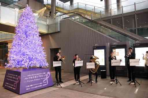 平成音楽大金管アンサンブルの演奏に合わせて点灯したパープルリボンツリー＝１２日、熊本市西区