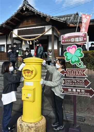 おかどめ幸福駅で、幸せをイメージした黄色い郵便ポストを拭く県立大の学生ら＝あさぎり町