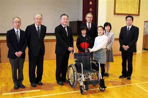 熊本善意銀行の和田浩二専務理事（左から３人目）から車いすを受け取る南阿蘇西小の児童ら＝南阿蘇村