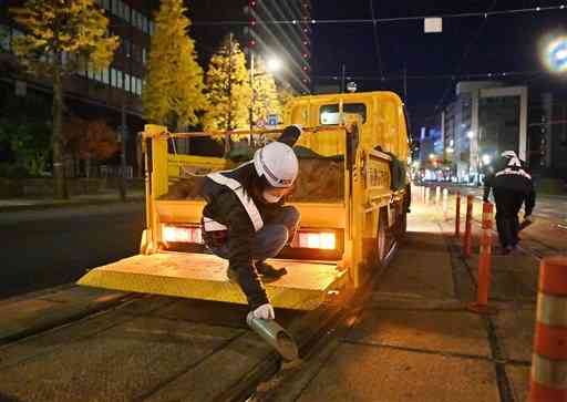 熊本市電の軌道に滑り止めの砂をまく職員＝２９日午前５時３５分ごろ、熊本市中央区（高見伸）