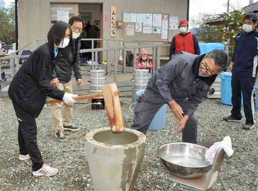 市民球場仮設団地の住民らと一緒に餅をつく、ボランティアで参加した八代高の女子生徒（左）＝八代市