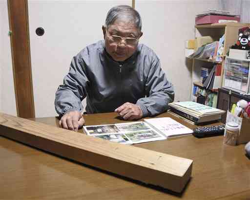 懐かしそうに写真を見返す日當國弘さん。手前は豪雨で全壊した球磨村神瀬の自宅から持ち出した柱。息子や孫の背丈が記録されている＝２０２１年１２月６日、人吉市