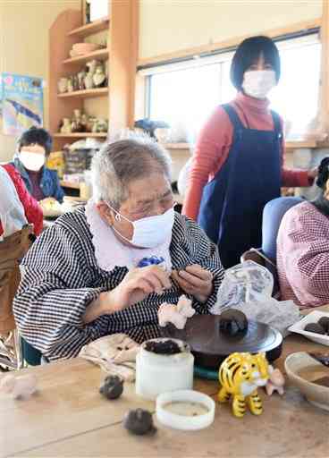 陶芸用の粘土で牛の箸置きを作る小川ハツ子さん（手前）。右後方は小川さんをサポートする愛隣館の境喜美代さん＝山鹿市