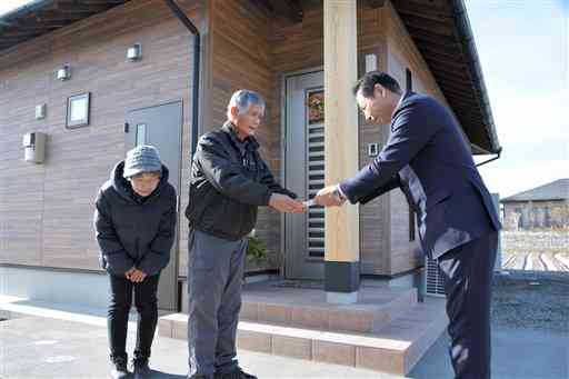 豪雨後に移転新築した自宅前で、吉松啓一村長（右）から補助金の目録を受け取る西村俊則さん、ユリ子さん夫妻＝相良村