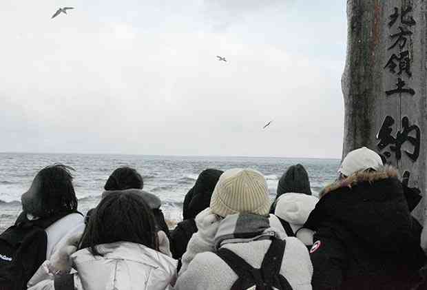 納沙布岬から歯舞群島を眺める熊本県の児童生徒。この日は肉眼でうっすらと確認できる程度だった＝２０２１年１２月、北海道根室市