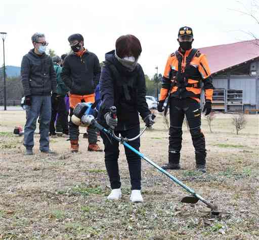 若手林業者（右）の指導を受けながら草刈り機の使い方を学ぶ女性移住者（中央）＝山鹿市