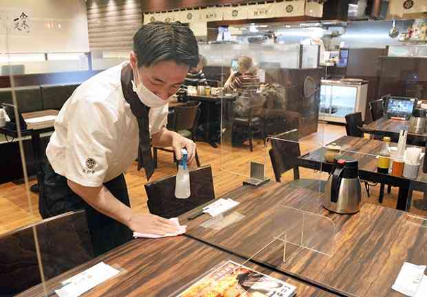 「とんかつ勝烈亭アミュプラザくまもと店」で、テーブルを消毒する従業員＝１８日、熊本市