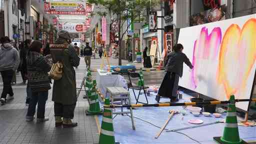 下通アーケードで開かれたイベントで、買い物客らが立ち止まって見る中、公開制作に取り組むしまうちみかさん＝熊本市中央区