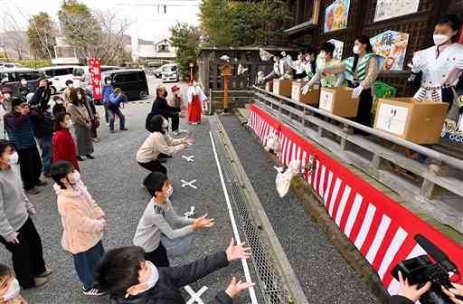 地元の小学６年生が投げる豆を間隔を空けて受け取る参拝客＝３０日午後、玉名市の疋野神社