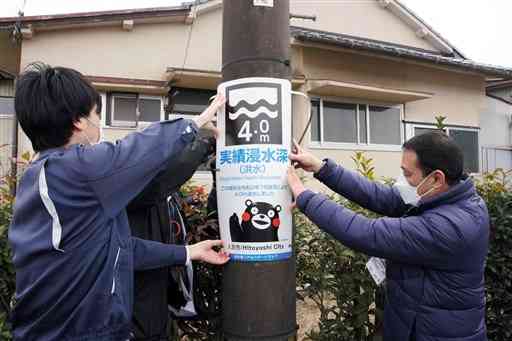 ２０２０年７月の豪雨で浸水した深さを示す表示板を設置する市職員＝人吉市