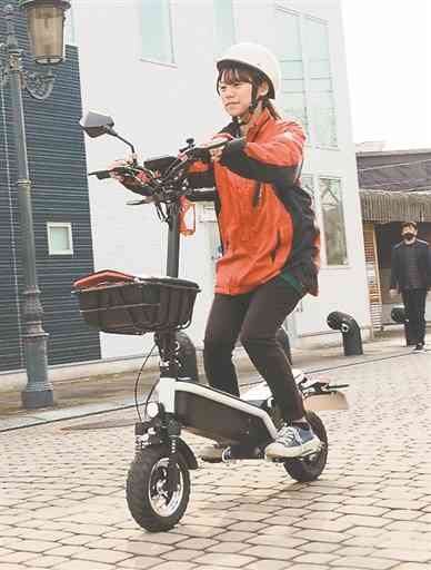 電動キックスケーターを運転する女性。免許証携帯が必要で、ヘルメットを着用して車道を通行する＝八代市