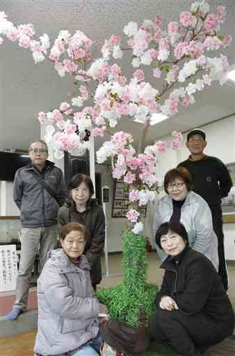 託麻西小玄関で、手作りした桜の木を囲む民生委員ら。右奥が宮崎敏幸会長＝熊本市東区