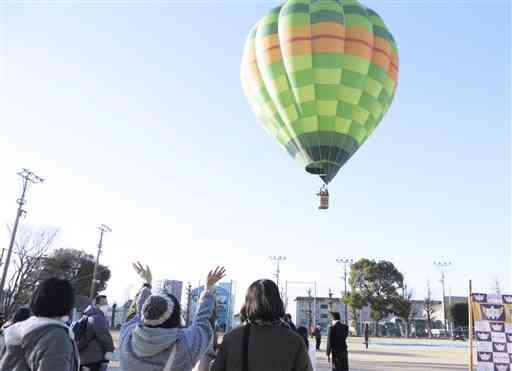 熱気球に搭乗した卒業生に地上から手を振る保護者ら＝熊本市東区