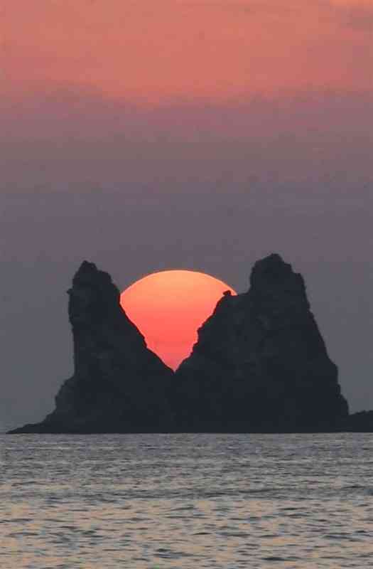 小ケ瀬の岩の間に沈む夕日＝天草市