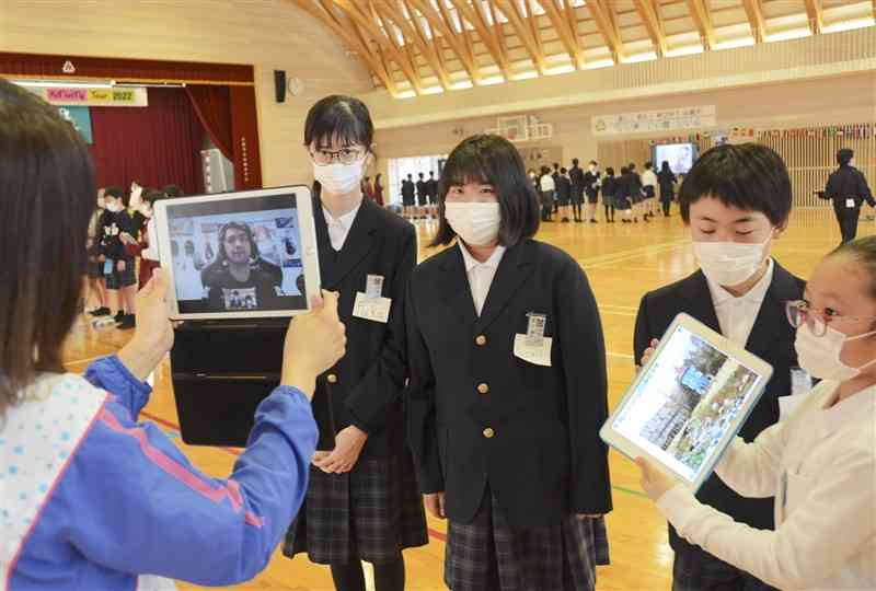 タブレット端末（左）の画面越しに英語で交流する山鹿小の児童ら＝山鹿市