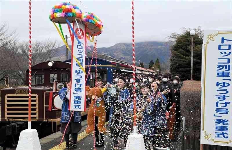 くす玉を割ってトロッコ列車の出発を祝う「０９６ｋ熊本歌劇団」のメンバーら＝１９日午前、高森町