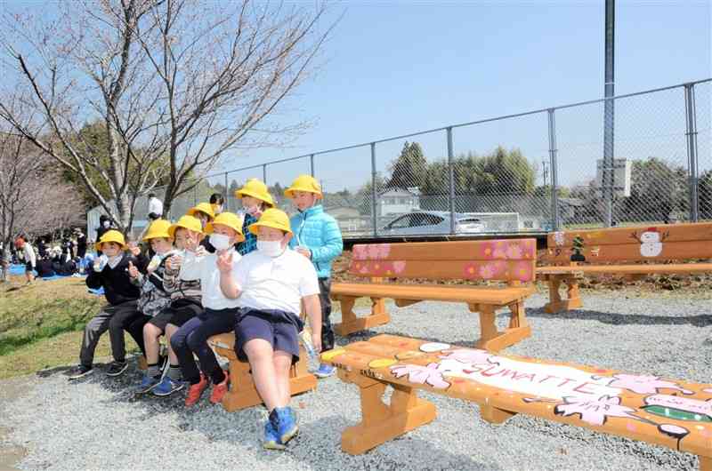 卒業した6年生が作ったベンチに腰掛けて記念写真に納まる西合志第一小の児童ら＝合志市