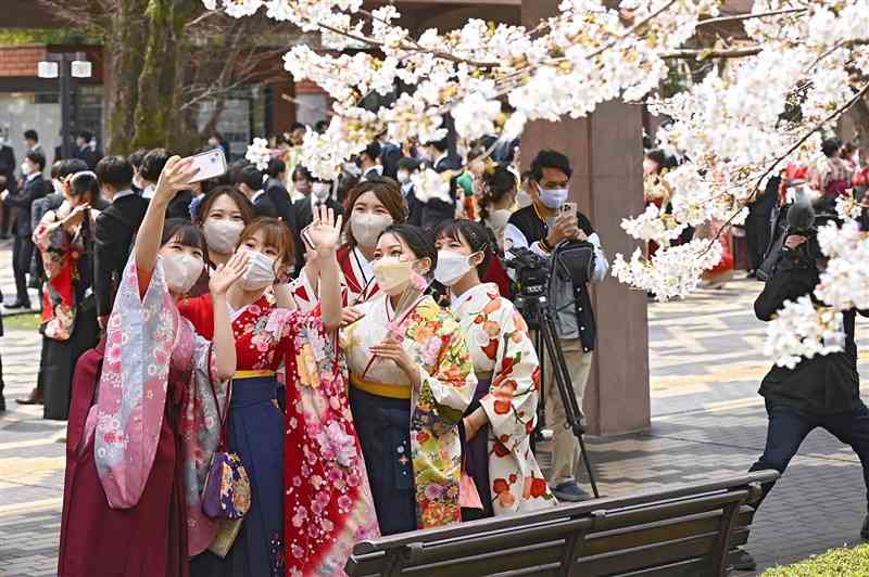 熊本大の卒業式後、桜の下で記念写真を撮る卒業生＝25日午前、熊本市中央区の県立劇場（小野宏明）