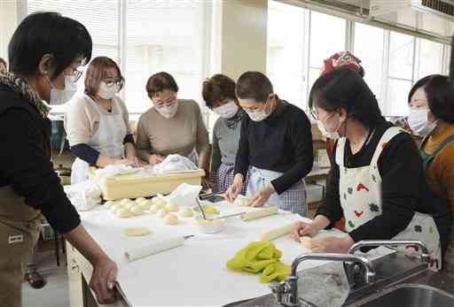 八代市働く婦人の家のパン教室で、講師の木本早苗さん（左から５人目）の実演を見学する生徒ら＝同市