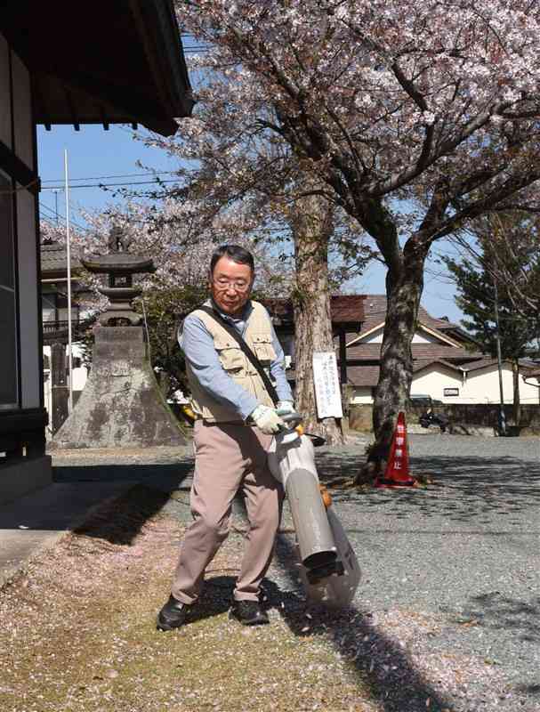 境内に散ったサクラの花びらなどを集める有働一敏さん。送風機は清掃作業軽減のため、地元住民が購入してくれた＝山鹿市