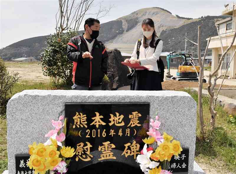 旧長陽西部小学校に作られた熊本地震慰霊碑の前で古庄幸男区長（左）の話を聞く東有咲記者。奥は立野の大規模崩落斜面＝6日、南阿蘇村（谷川剛）