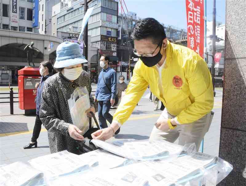 県支部新聞公正取引協議会のメンバー（右）から新聞を受け取る買い物客＝9日、熊本市中央区