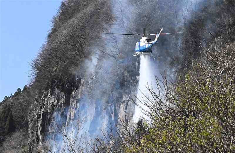 煙を上げる斜面へ放水する宮崎県の防災ヘリ＝9日午後4時20分ごろ、高森町