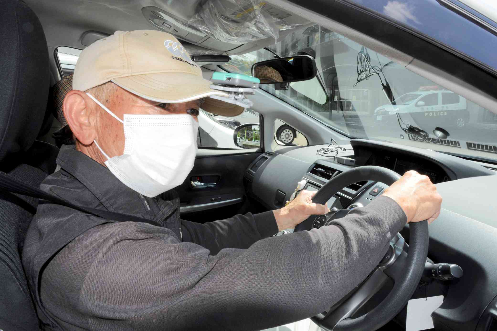 運転技能自動評価システムで運転動作を測定する高齢者。帽子のつばにセンサーを付けている＝人吉市