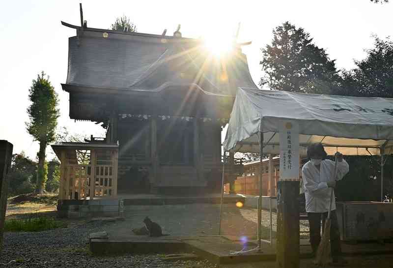 熊本地震で被災し、昨年12月に再建した益城町の木山神宮の神殿。朝日を浴びながら境内の清掃をしていた権禰宜（ごんねぎ）の矢田秋代さんは「神宮と同じく町の復興も進んでほしい」と願う＝13日午前7時半ごろ（後藤仁孝）