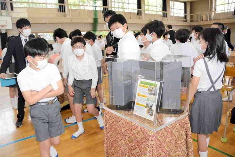 液状化対策工事に使う鋼鉄製の矢板を興味深そうに見つめる日吉小の児童たち＝熊本市南区