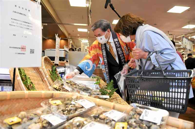 鶴屋百貨店の特設売り場で、買い物客に県産アサリをPRする蒲島郁夫知事（奥）＝17日、熊本市中央区