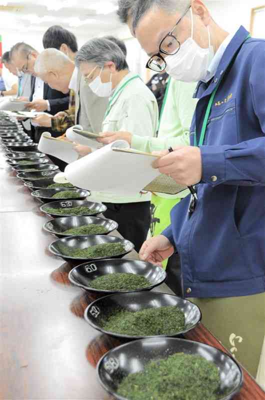 県産一番茶の初入札会で、出品された茶葉の手触りや香りを確かめる販売業者ら＝21日、益城町