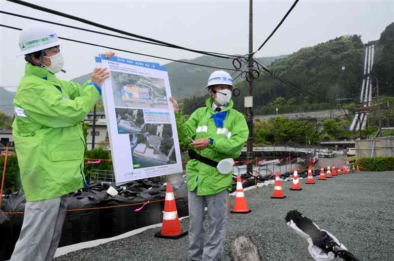 水圧管路の復旧工事について説明する九電水力開発総合事務所の担当者。右奥に見える既設の旧水圧管路は大部分を撤去し、新設する＝21日、南阿蘇村