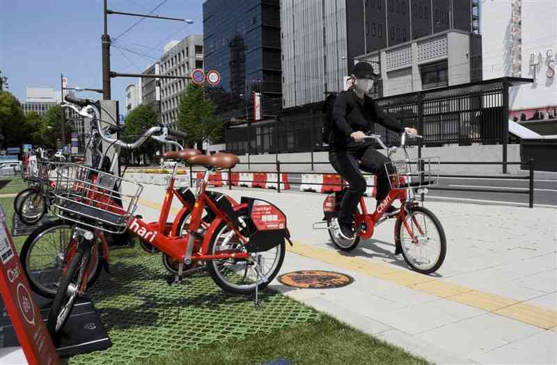 シェアサイクルのポート（置き場）から自転車に乗って走り出す利用者＝熊本市中央区