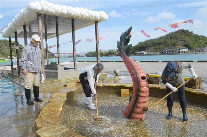 合津港にある「龍の足湯」をブラシで磨き上げる今津地区まちづくり委員会のメンバー＝上天草市