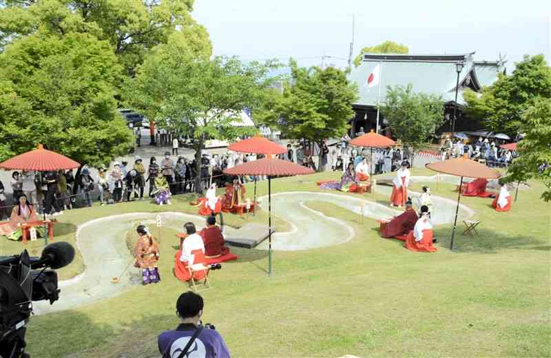 庭園内になる小川のふちに座り、和歌を詠む歌人ら＝熊本市北区