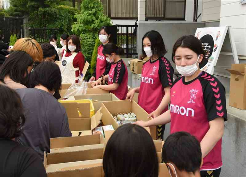 「山鹿こども食堂百華」の慈善イベントに集まった親子連れに食品を無償配布するオムロンの選手たち＝山鹿市