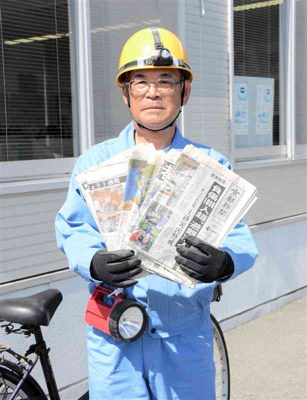 熊本地震を報じる京都新聞を持つ永野久治さん。身に着けている作業着やヘルメットは就寝時、枕元に常備している＝熊本市東区