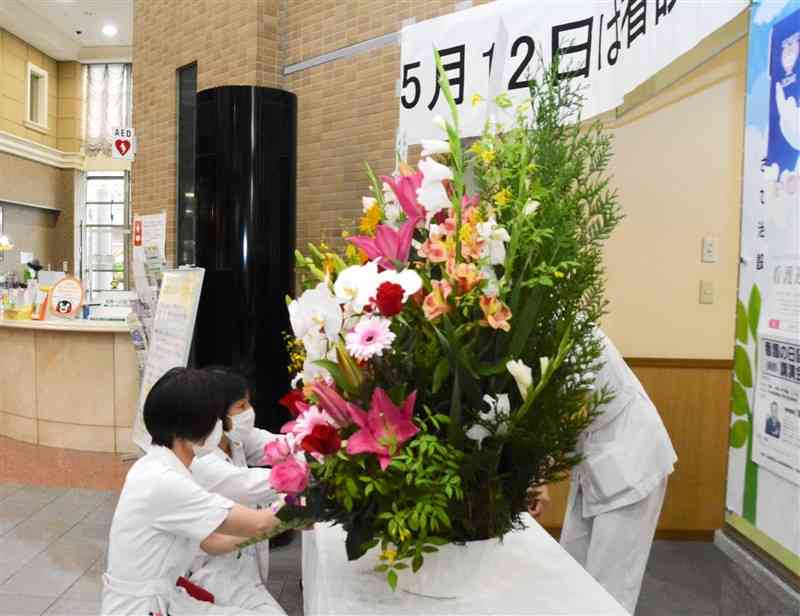 「看護の日」を前に、ナイチンゲール像の周りを花で飾る看護師＝熊本市東区