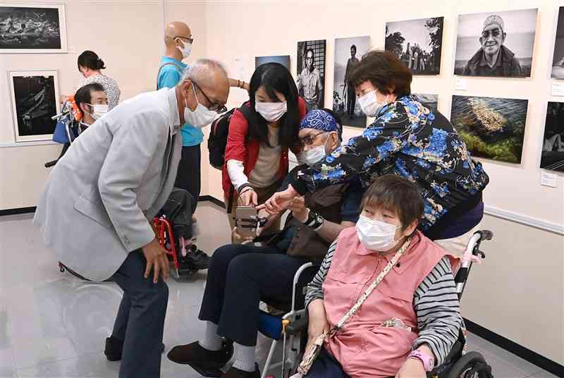 写真家の芥川仁さん（左手前）とともに「9人の写真家が見た水俣」展に見入る胎児性や小児性の水俣病患者ら＝14日、熊本市中央区の新聞博物館（小野宏明）