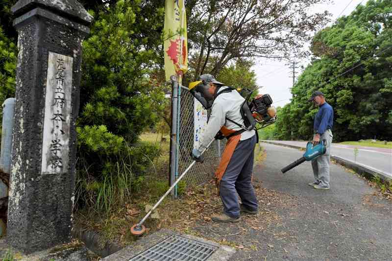 府本小校門付近の草を刈る府本地区協議会のメンバー＝荒尾市