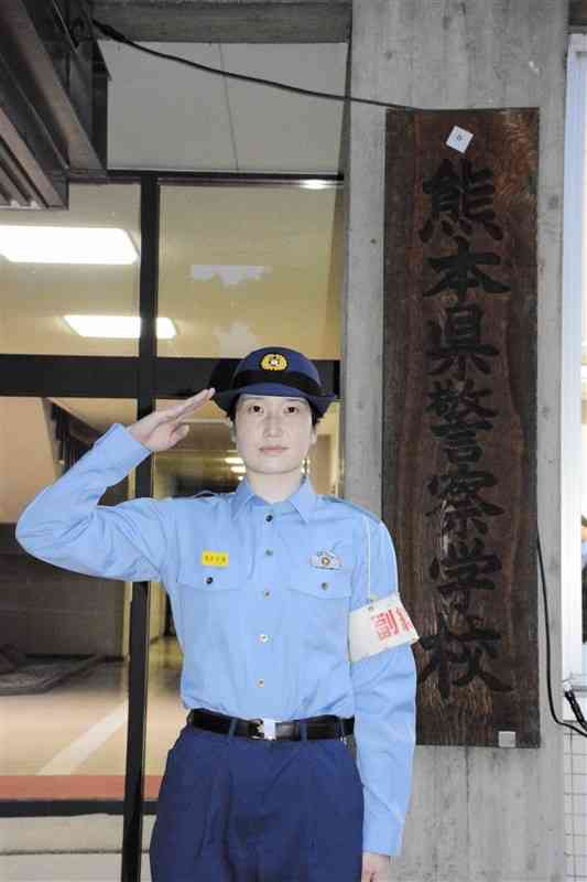 県警察学校の看板の前で敬礼する金子仁美さん＝熊本市中央区