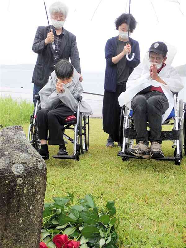 原田正純さんをしのび、石仏に赤いバラを手向けて祈る水俣病患者ら＝11日、水俣市
