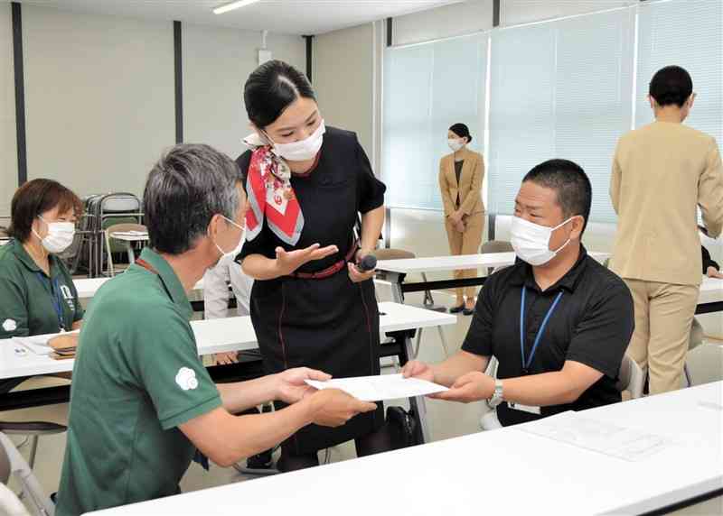 空港業務スタッフ（中央）から、丁寧な物の渡し方を学ぶ益城町職員＝同町