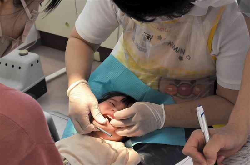 1歳6カ月児の健診で、口の中のチェックを受ける子ども。正しい仕上げ磨き方法などを保護者に伝えている＝6月23日、熊本市東区