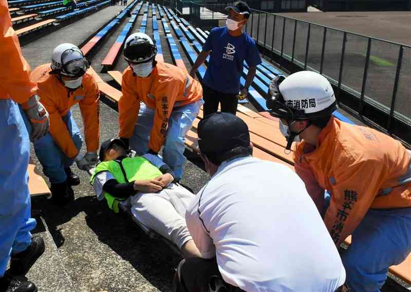 熱中症の対応訓練で観客席から患者役を運ぶ消防隊員ら＝1日午前、熊本市中央区のリブワーク藤崎台球場