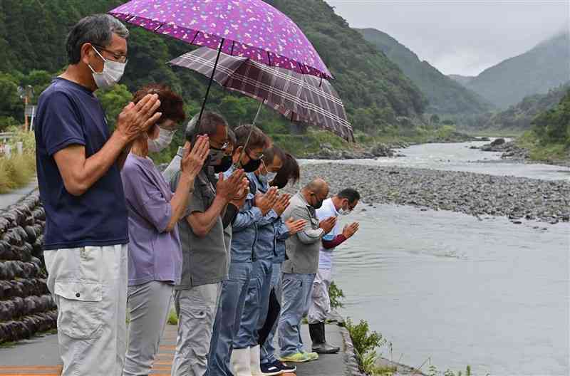 豪雨災害追悼のサイレンに合わせ、球磨川に向かって手を合わせる住民ら＝4日午前8時半ごろ、球磨村（後藤仁孝）